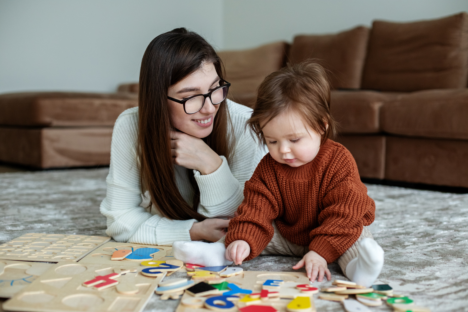 Mother and little daughter play educational games on rug in